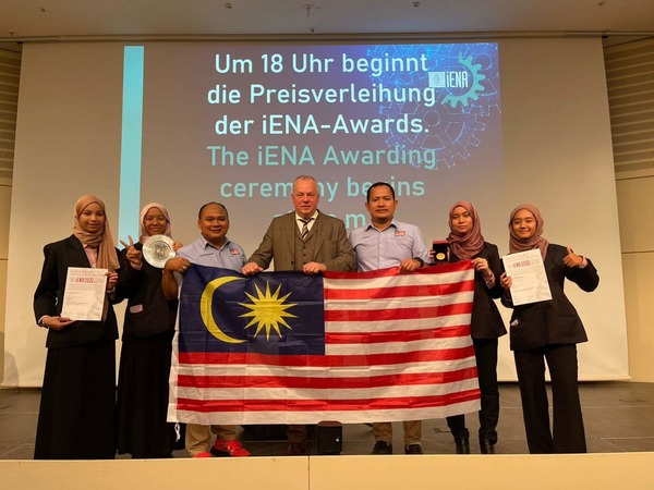 The team posing with their teachers on stage with the Jalur Gemilang displayed.