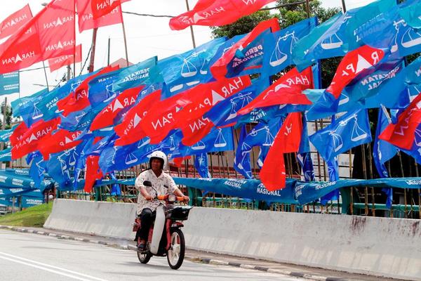 Photo shows a man on a kapcai riding through a street covered with coalition flags.