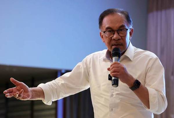 The photo shows Anwar in a white shirt and speaking into a handheld mic.