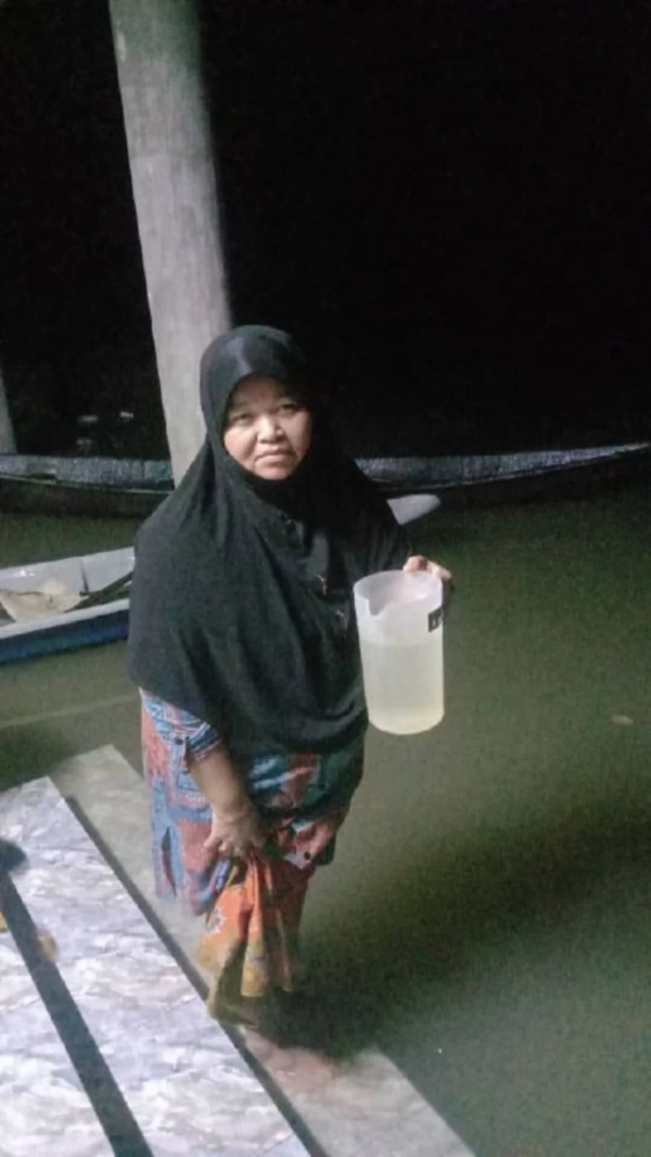 Muzipah Che Muda with a jug of floodwater.