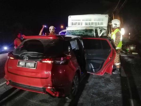 Photo of the accident, showing the red Toyota Yaris in collision with the lorry. There are firemen standing around the vehicles.