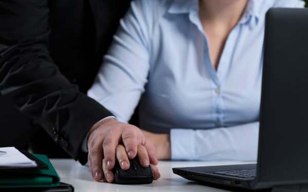 Image of a male colleague touching a female colleague under the pretext of helping at work for illustration purposes only.