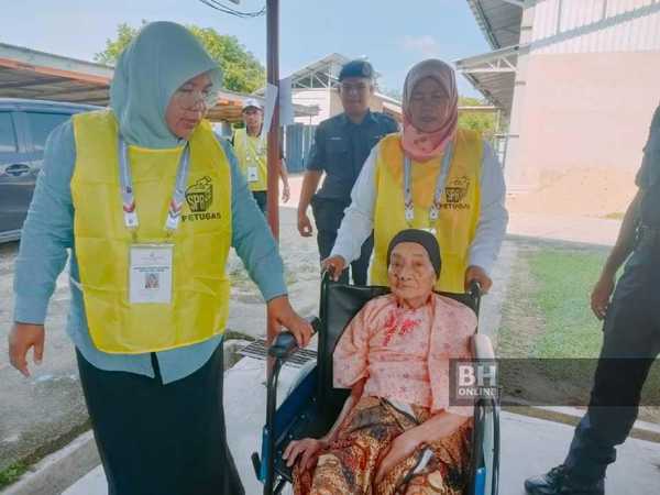 Munah Adam (in a wheelchair) being assisted by an Election Commission officer.