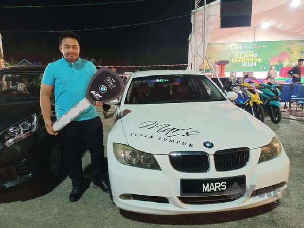 Mohamad Helmi Mohammad posing for a photo with his lucky draw prize, a BMW 320i.