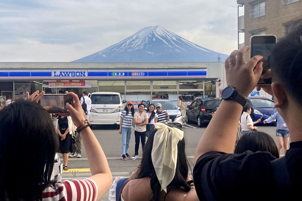 Tourists are seen taking photos of Mount Fuji appearing over a convenience store in Fujikawaguchiko town.