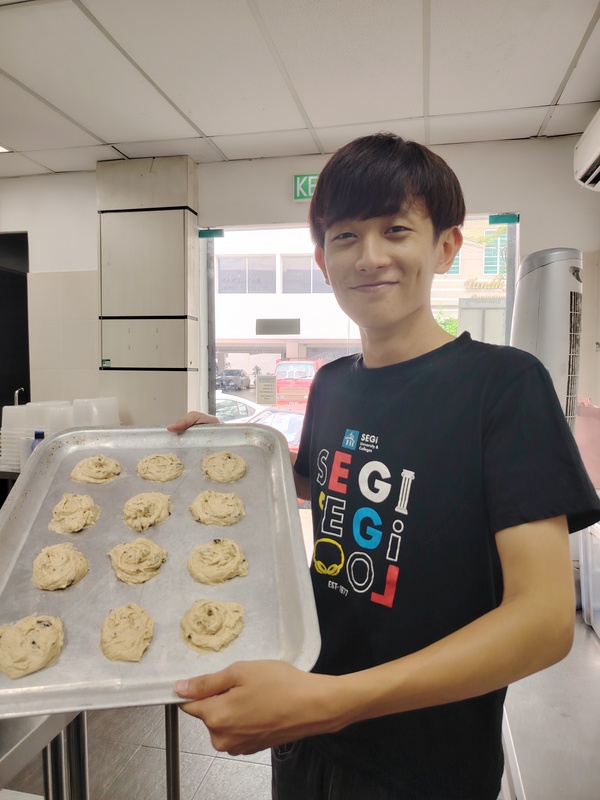 A SEGi College culinary student proudly presents a tray of banana chocolate chip cookies, showcasing the success of their previous culinary efforts using surplus ingredients.