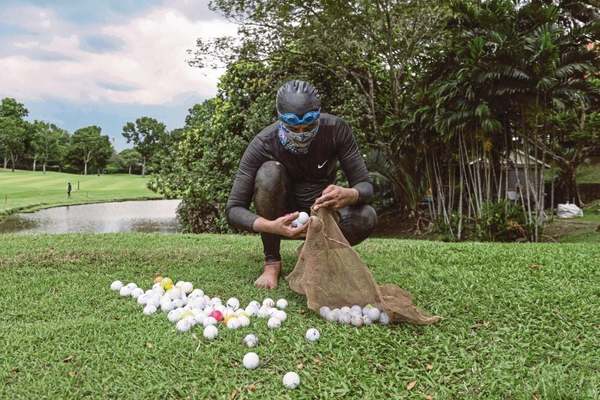 Sumadi places golf balls he recovered from a pond into a net at a golf course in Shah Alam, near Kuala Lumpur.