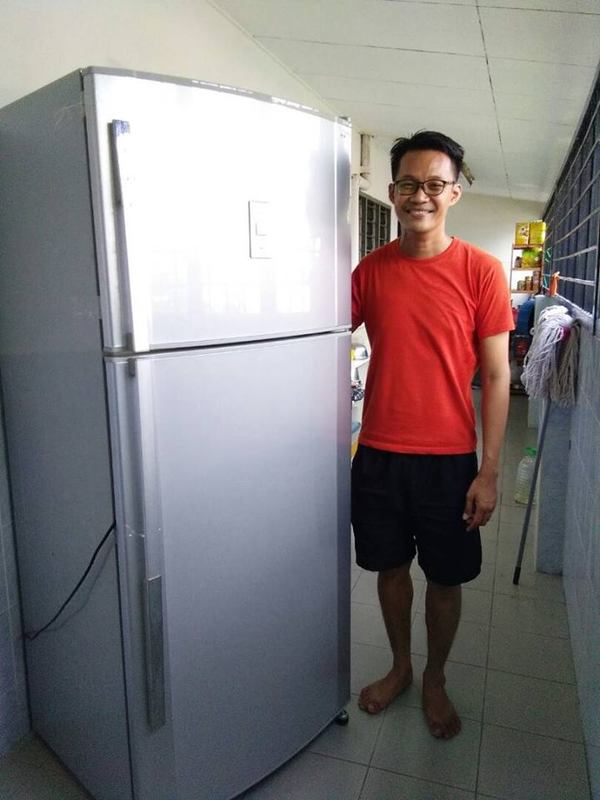 red chinese man with spectacles standing next to a silver hitachi refrigerator