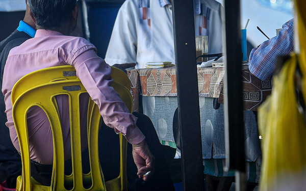 A man attempts to conceal his cigarette as health officers approach his table in Kuala Lumpur yesterday, 1 January.