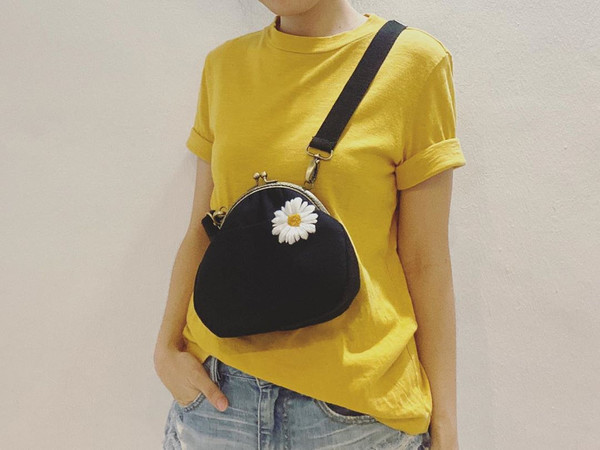 A black sling bag with an embroidered daisy.