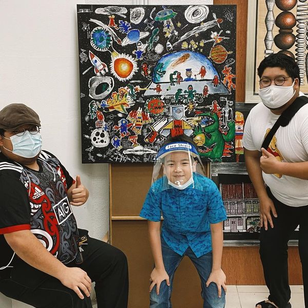 Rayyan (centre) at an art booth posing with his masterpiece, titled 'Space Wars'.