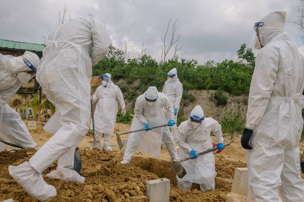 Healthcare workers wearing personal protective equipment burying a deceased COVID-19 patient.