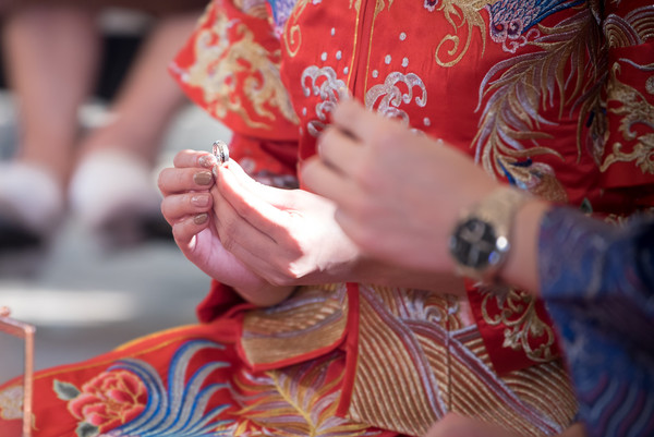 Bride and groom dressed in traditional Chinese wedding attire while holding their wedding rings.