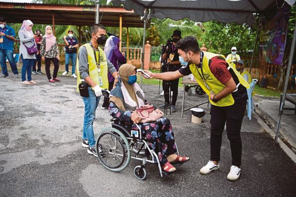 An Election Commission worker checking the temperature of a voter at SK Durian Daun, Melaka during the state election.