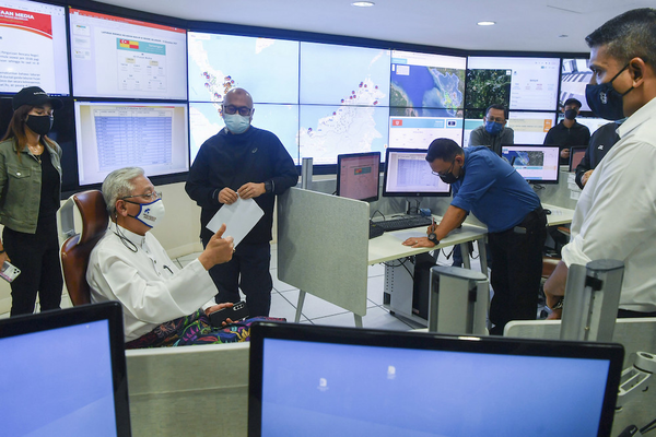 Prime Minister Ismail Sabri (sitting) being briefed on the country's flood situation by Aminuddin (standing next to him) at the National Disaster Control Centre (NDCC).