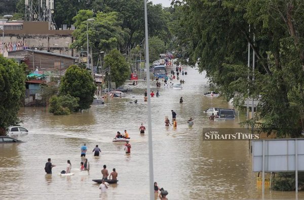 People wading through the floodwaters in Jalan Bukit Kemuning near Taman Sri Muda on 19 December 2021.